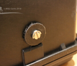 Flat Head D-ring 1/4" Mounting Screw, screwed through case and fixing mounting plate. I created a spacer, using a disk cut out of the plastic circle originally cut to create the lens aperture. This was needed as the screw shaft is quite long. img 5199